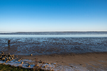 Ein Mann steht mit Stativ und Kamera im Watt im Winter in Keitum, Insel Sylt