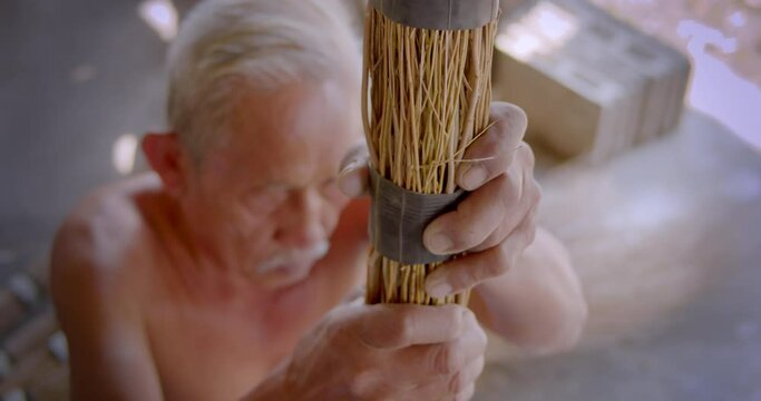 Asian male farmer who is an elderly person makes brooms from the grass that has many names called Paddy's lucerne, Queensland hemp , Arrowleaf sida , Common sida , Cuba juite for extra income.