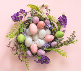 Easter decoration, egg nest on pink background. Festive flower wreath full of pastel color egg.
