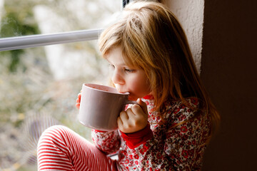 Little preschool girl holding cup with hot chocolate with marhsmallows. Happy child in pajamas...
