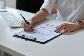 Cropped view of businesswoman's hand working in the office holding a pencil working on a graph data working in the office. For marketing and business concept