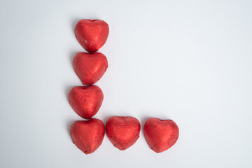 Chocolate red heart sweets in the shape of the letter L for Valentine's Day on a white background