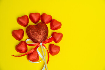 Chocolate red heart sweets for Valentine's Day on a yellow background in the shape of a circle with a heart decoration on a wooden pole in the middle.