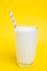 Glass of milk with purple straw isolated on yellow background