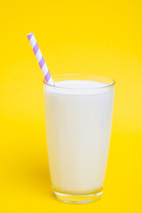 Glass of milk with purple straw isolated on yellow background