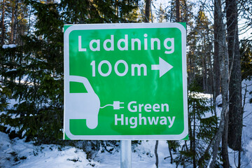 Fototapeta premium Sundsvall, Sweden A green street sign pointing towards an electrical charging station for cars. Laddning in Swedish means charging.