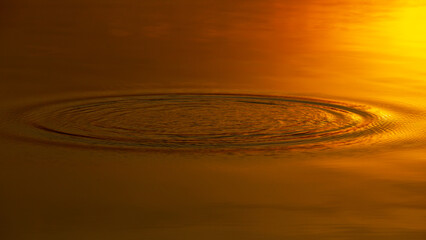 Water ripple circle on the surface of lake water with reflection of sky clouds at sunset or evening time.