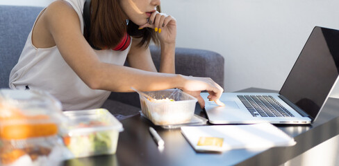 Woman eating lunch while working on laptop at home during the day. Work from home and social distancing concept for quarantine.