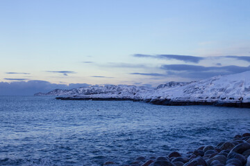 Winter seascape. Snow-covered rocky shore. Sea and blue sky. Russia, Teriberka, Kola Peninsula.