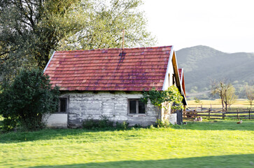 Old Wooden Village Farm House with Grass and Fence in  Croatian Countryside. Natural Environment with Meadow and Mountains in Background