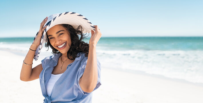 Smiling beautiful latin woman on beach with straw hat at sea