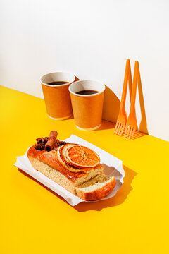 Orange and cinnamon pond cake, coffee in paper cups, two bamboo forks on vibrant yellow background