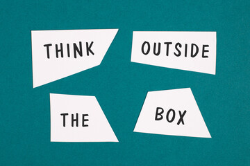 Think outside the box is standing on pieces of white paper, petrol colored background,...