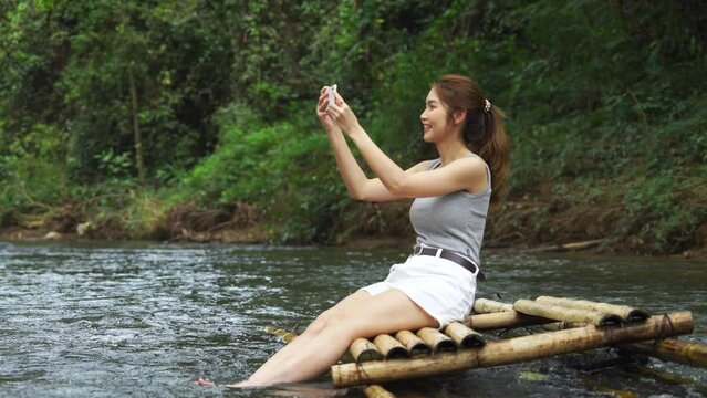 Young asian woman sitting on a bamboo raft taking photos of beautiful view.