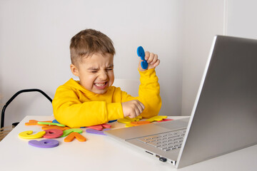 Little boy learning alphabet and numbers online, with laptop at home. Child is sad and stressed....