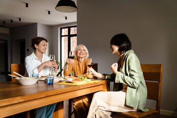 Mature three women drinking wine while having dinner in kitchen