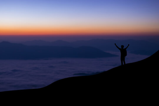 Silhouette of young traveler and backpacker standing and open arm watched foggy landscape and mist alone on top of the mountain. He enjoyed traveling and was successful when he reached the summit.