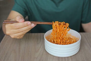 a man in a green t-shirt hold chopsticks with korean style instant noodles. K-pop became a global...