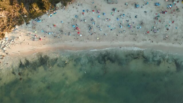 Aerial truck left of people resting in the sand near sea shore and pine woods at sunset in El Canelillo beach, Chile