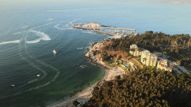 Aerial dolly in flying over turquoise sea shore, near Pajaros Ni&ntilde;os sanctuary islet and woods, El Canelillo beach, Chile