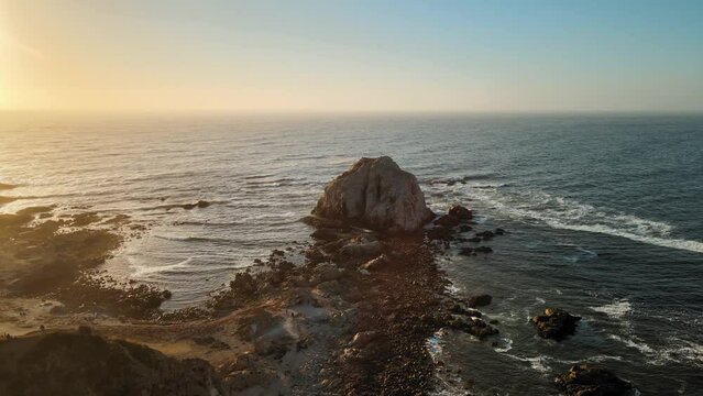 Aerial dolly in of Pe&ntilde;a Blanca islet and sea waves hitting rocky shore at golden hour in El Canelillo beach, Chile