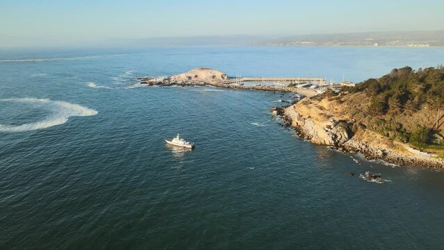 Aerial dolly in of ship sailing in sea near Pajaros Ni&ntilde;os sanctuary islet in rocky shore at sunset, El Canelillo beach, Chile
