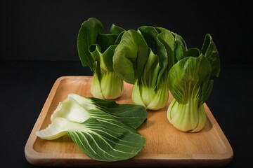 Organic green Baby Bok Choy or Brassica rapa chinensis on wooden plate on black background. Popular...