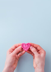 Valentine's day background. Women's hands hold a pink knitted heart made of threads on a blue background. Close-up. The concept of a holiday and relationships. Flat lay, copy space