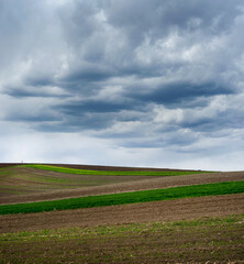 Fototapeta na wymiar Colored lines and hills of spring fields under a beautiful storm sky with contrasting clouds.