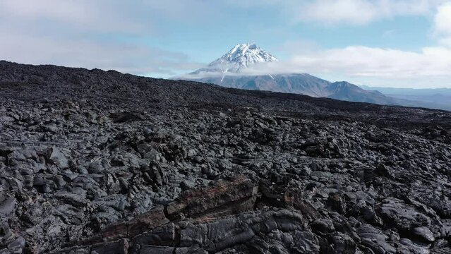 Black frozen lava flow from crater on the slopes of  Tolbachik volcanoes, on background Bolshaya Udina volcano, Kamchatka, Russia