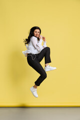 Fototapeta na wymiar Studio shot of young cheerful girl wearing casual style clothes jumping isolated on yellow background. Concept of emotions