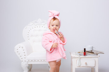 A cute little baby girl in a pink terry dressing gown with a chair and a mini dressing table with...