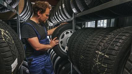 Naklejka na ściany i meble tire at repairing service garage background. Technician man replacing winter and summer tyre for safety road trip.