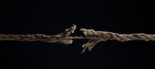 A stretched rope breaks on a black background. The concept of divorce. A break in a relationship. - obrazy, fototapety, plakaty