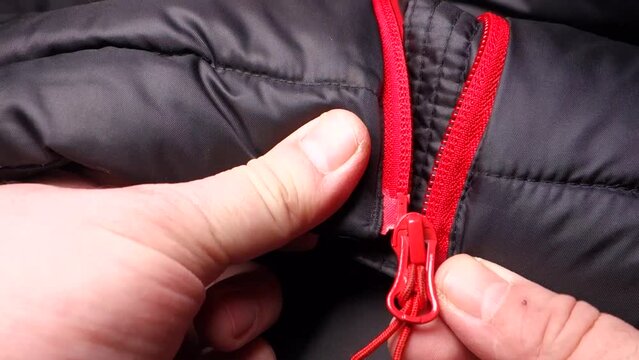 Zipping the red zipper of the black winter jacket by hand