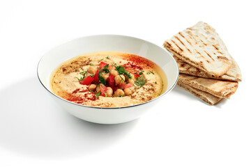 Hummus with spices, chickpeas, tomatoes and pita bread in a bowl isolated on a white background