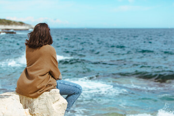 Fototapeta na wymiar woman sitting on cliff enjoying view of the sea. windy weather. sunny day