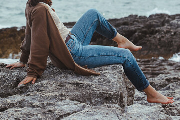 woman walking by rocky sea beach in wet jeans lighthouse on background