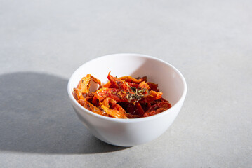 dried tomatoes with spices in a white plate on a gray concrete background