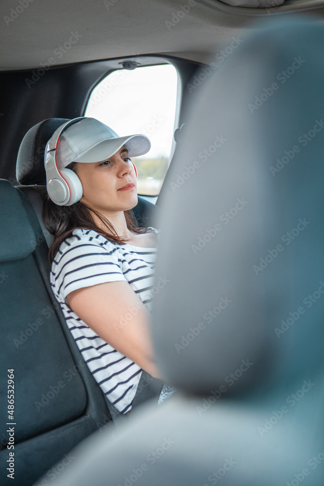 Poster woman sitting at car rear sits listening music with headset