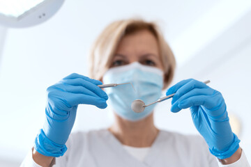 Dentist in mask and gloves holding stainless instruments