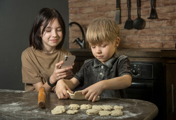 Naklejka premium the girl takes pictures on her smartphone as her brother makes cookies