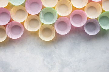 moldes de papel de colores para cupcakes o magdalenas, alineados sobre un fondo gris claro, con espacio en blanco