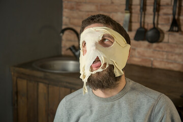 a young man with a beard rolls out dough on cookies and indulges, makes a mask of dough on his face