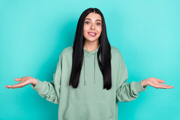 Photo of stressed millennial brunette lady shrug shoulders wear green hoodie isolated on turquoise...