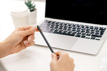 A woman with a pencil in her hands is sitting in front of a laptop screen.Rear view, female hands and laptop screen close-up.Business concept.Copy space,selective focus