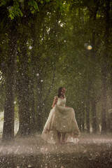 happy bride in a white wedding dress in the rain on an alley under big green trees walking peaying sitting and laughing