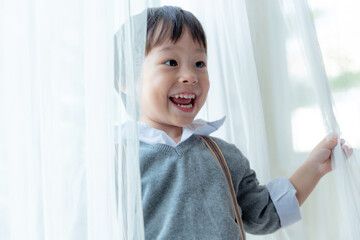 Happy cute little boy fun and enjoying playing and smiling with white curtain.