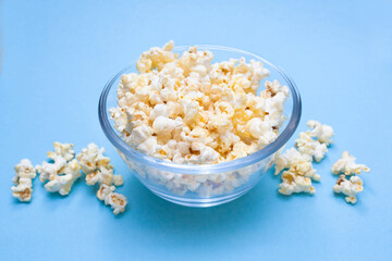 Popcorn on a blue background. Blue background. Movie watching concept. Popcorn in a glass bowl for watching a movie and series. Quick and tasty snack.