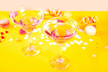 Glasses of pink cocktails with heart candies on yellow background. Birthday party or Valentines day concept.